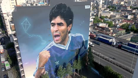 Street-art-celebrating-Argentine-soccer-legend-Diego-Maradona-on-his-second-anniversary,-a-giant-wall-mural-appeared-in-the-sky-in-downtown-Buenos-Aires,-Argentina,-aerial-descending-close-up-shot