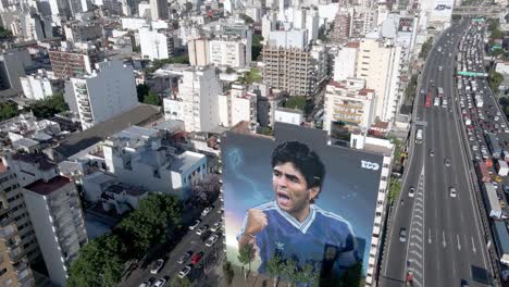 Diego-Armando-Maradona's-second-death-anniversary,-a-giant-wall-mural-popped-up-in-the-sky-of-downtown-Buenos-Aires,-neighborhood-of-constitucion,-aerial-panning-urban-cityscape-view