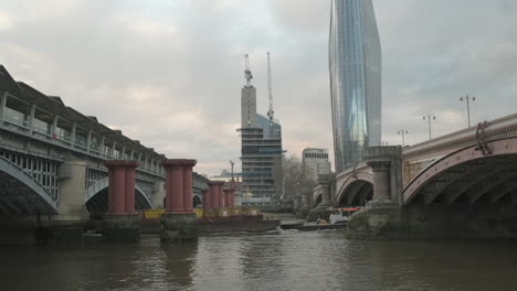 Bankside-Yards-Development-Under-Construction-in-London-with-One-Blackfriars-Building,-Blackfriars-Bridge-and-Train-Station,-Tug-boat-pulling-Shipping-Containers-up-the-Thames