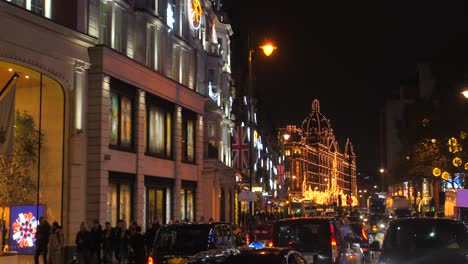 Pan-shot-of-famous-brompton-road-with-Harrods-department-store-decorated-for-Christmas-with-crowded-sidewalk-and-heavy-traffic-movement-at-night-time