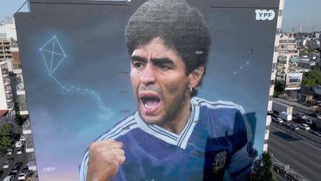 Maradona-mural-in-neighborhood-of-Constitucion-painted-by-Martin-Ron-to-commemorate-the-World-Cup-legend,-aerial-pull-out-shot-away-from-the-building-wall,-capturing-the-cityscape-of-Buenos-Aires