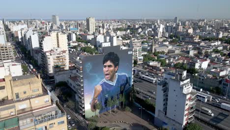 Cityscape-of-Buenos-Aires-with-a-giant-wall-mural-of-Maradona,-aerial-look-down-descending-shot-capturing-perfect-depiction-of-the-respectful-late-soccer-player-by-street-artist-Martin-Ron