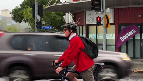 Aussie-male-cyclist-wearing-magpie-cycling-helmet-with-cable-ties-spotted-on-the-road,-to-deter-swooping-bird,-rainy-day-at-Bowen-Hills,-Brisbane-city,-Queensland,-Australia
