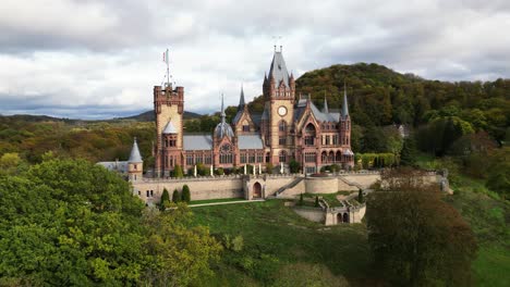 Panorama-shot-of-the-front-of-the-Drachenburg-Castle-situated-in-the-Drachenfels,-Königswinter,-Germany-with-a-beautiful-autumn-sun-and-coloured-leaves