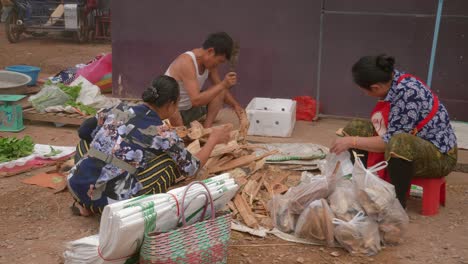 Local-asian-people-seated-on-ground-cutting-wood-for-selling-in-street
