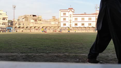 Vista-Desde-La-Línea-Lateral-De-Jugadores-De-Fútbol-Corriendo-En-Un-Partido-Local-En-Karachi,-Pakistán