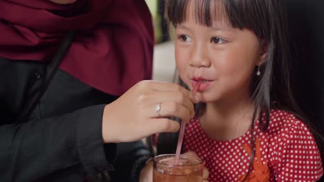 Mom-helps-little-asian-child-drinking-sweet-ice-tea-at-restaurant-Nasi-Jamblang-Traditional-rice-dish-typical-culinary-form-Cirebon,-West-Java,-Indonesia