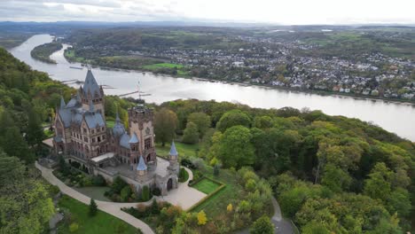 Panning-shot-of-the-Drachenburg-Castle-on-the-Drachenfels-hills-in-Königswinter-with-the-river-Rhein-in-the-background-on-a-cool-autumn-day