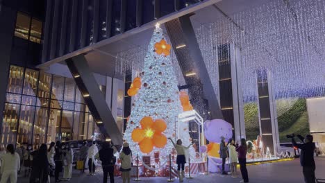 Gran-árbol-De-Navidad-Blanco-Con-Flores-Naranjas-Instalado-Cerca-Del-Hotel-Conrad-Por-La-Noche-Con-Chinos-Tomando-Fotos