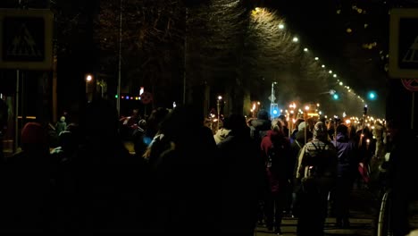 People-going-in-a-patriotic-torchlight-procession-in-Liepaja-city-on-Lacplesa-day-,-autumn-evening,-city-landscape,-traffic-lights,-wide-shot