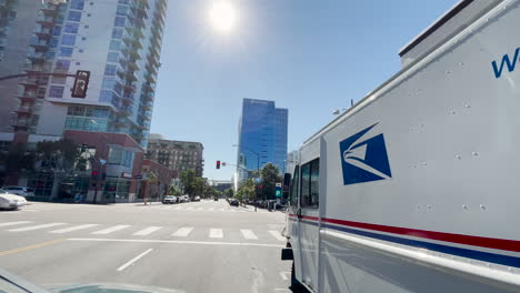 Driving-by-a-USPS-delivery-truck-parked-on-the-side-of-the-road-in-downtown-San-Diego,-California