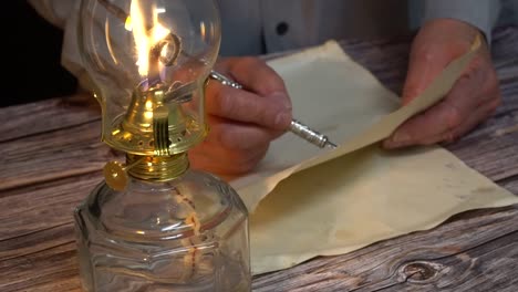 Person-writing-with-a-vintage-quill-pen-next-to-an-oil-lamp