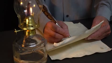 Person-writing-with-quill-pen-next-to-an-oil-lamp