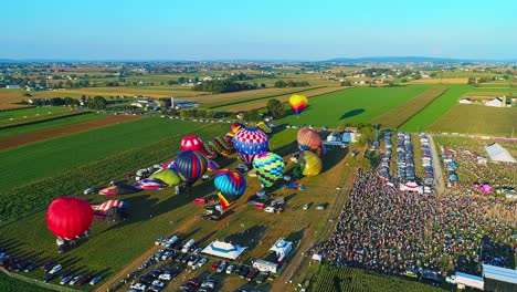 An-Aerial-View-of-Multiple-Hot-Air-Balloons-Launching-into-the-Sky-During-a-Festival-With-Crowds-Watching,-on-a-Summer-Day
