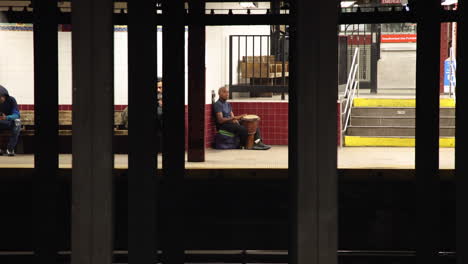 Male-Busker-Drumming-On-Station-In-New-York-Viewed-From-Across-Platform