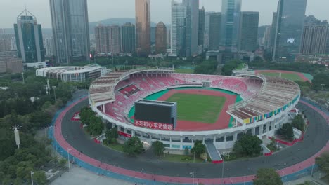 Estadio-De-Fútbol-Del-Centro-Deportivo-Tianhe-En-Guangzhou-Por-La-Noche-Con-Plaza-Cítica-Y-Torres-De-Oficinas-Comerciales-En-Segundo-Plano