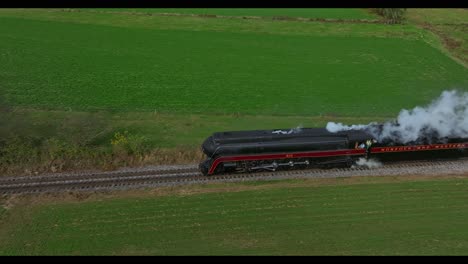 Drone-Parallel-View-of-a-Steam-Passenger-Train-Blowing-Smoke-and-Steam-Crossing-a-Crossing-with-Spectators-Watching-on-a-Sunny-Fall-Day