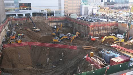 Circling-Excavation-Site-In-New-York-City-With-Yellow-Excavators,-Construction-Site-Rubble,-And-Construction-Workers-Walking-Around