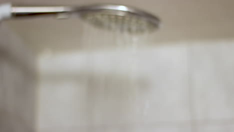 Seitenansicht-Eines-Defokussierten-Duschkopfs-Mit-Herunterlaufendem-Wasser-Im-Badezimmer
