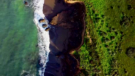 Flying-over-sunlit-waves-and-sand-beach-carved-out-of-tall-cliffs-in-California