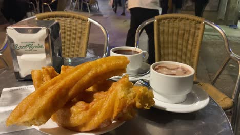 Close-up-of-some-porras-and-churros-with-hot-chocolate-at-a-table-in-the-street-of-the-old-bar-of-San-Gines,-Madrid