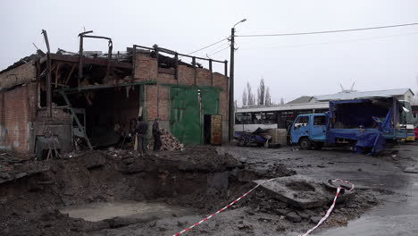 Workers-walk-past-a-Russian-S-300-missile-crater-that-has-filled-with-rainwater-in-front-of-a-destroyed-garage-and-vehicles-at-a-bus-depot