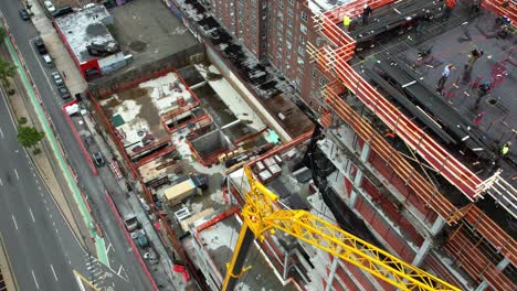 Crane-lifting-material-to-workers-on-top-of-a-structure-in-Queens,-NY---Aerial-view