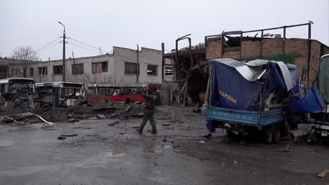 Workers-walk-past-a-Russian-S-300-missile-crater,-a-destroyed-garage-and-vehicles-at-a-bus-depot