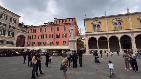 Panning-shot-of-people-at-Piazza-dei-Signori-popular-square-of-Verona-Italian-city-with-Dante-Alighieri-statue-in-center