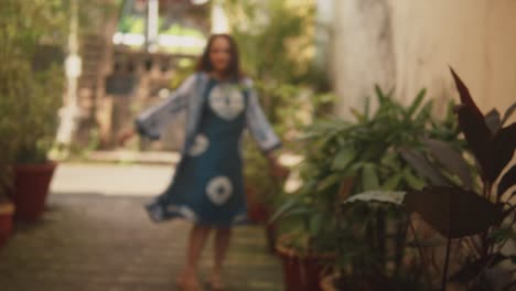 Out-of-focus-brunette-Indian-woman-walking-away-and-spinning-around,-next-to-some-plants,-in-the-historical-streets-of-Fontainhas,-India