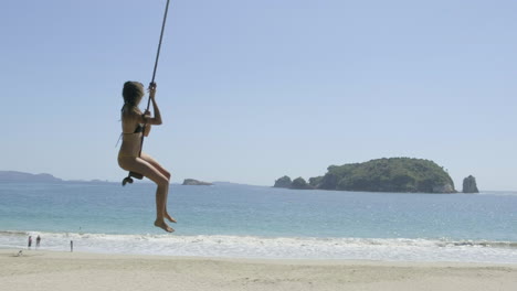 Girl-on-rope-swing-on-hahei-Beach,-New-Zealand