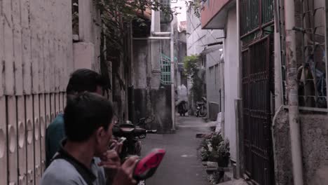 South-east-asian-men-sitting-in-an-alley-and-a-man-carrying-a-big-sack-of-goodies-using-a-motorbike,-somewhere-in-jakarta