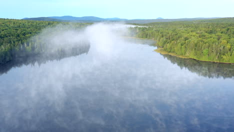 Aerial-drone-shot-rising-above-the-fog-and-mist-hanging-above-the-still-blue-waters-of-the-Spectacle-Ponds-in-the-Maine-wilderness