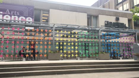 Steady-long-distance-shot-of-a-large-number-of-multiple-colored-paper-fans,-arranged-in-proper-pattern,-rotating-due-to-the-wind-displayed-at-Toronto-University-during-Pride-week,-during-day-time