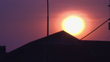 Time-Lapse-of-a-Circular-Ball-Sun-Setting-Behind-a-Silhouette-of-a-Roof-Top-of-a-Building