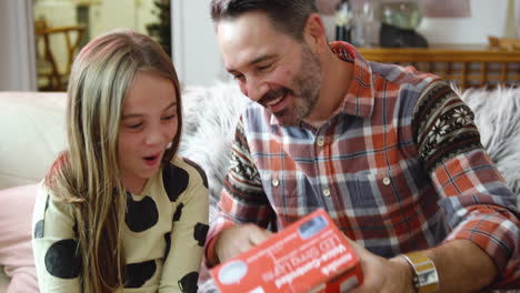Father-opens-Christmas-gift-form-his-daughter-while-smiling-at-her