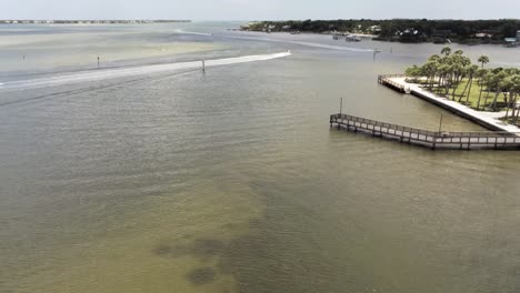 Aerial-view-of-boat's-moving-out-the-inlet-in-south-Florida,-wooden-pier-in-the-foreground