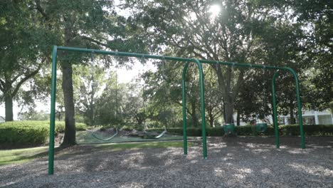 Empty-Swings-in-Playground-With-Sun-Shining-Through-Trees-in-Background-on-a-Summer-Day