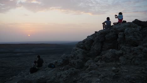 Steady-shot-of-people-sitting-on-a-rock-formation-while-watching-the-sunrise