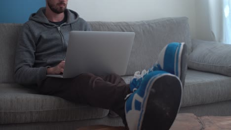 Man-sits-comfortably-on-couch-and-works-on-laptop-from-home