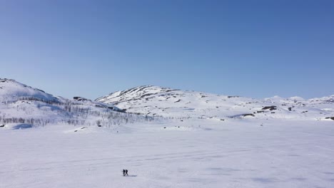 Luftaufnahme-Von-Menschen,-Die-über-Zugefrorenem-See-In-Verschneiter-Berglandschaft-Skifahren