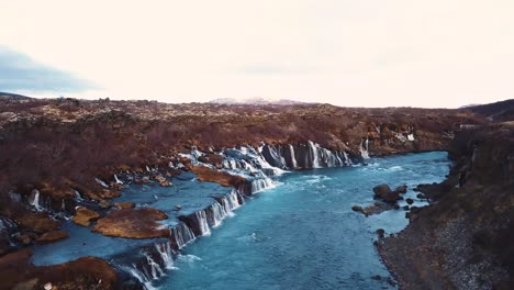 Drone-with-cinematic-movements-shows-beautiful-icelandic-waterfall,-Hraunfossar,-in-sunset-light-from-multiple-angles