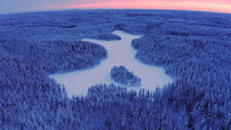 Drohnenaufnahme-Eines-Schneebedeckten-Waldes-Und-Eines-Eisigen-Sees-Mit-Gekrümmtem-Horizont-Zur-Goldenen-Stunde-Nach-Sonnenuntergang