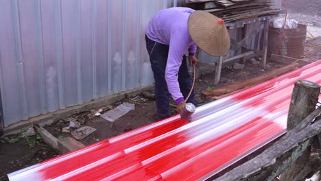 Asian-worker-using-spray-gun-to-paint-a-sheet-of-roof-metal