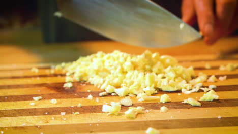 Garlic-is-being-minced-with-a-chef's-knife-on-a-striped-wooden-cutting-board