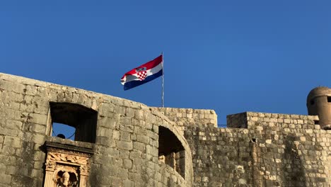 Etablierte-Aufnahme-Der-Kroatischen-Fahne,-Die-Auf-Der-Spitze-Der-Alten-Stadtmauern-Von-Dubrovnik-Weht,-Berühmter-Drehort-Von-Game-Of-Thrones