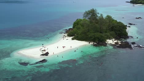 Aerial-view-drone-shot-of-peoples-on-a-tropical-small-island-with-trees,-rocky-and-white-sand-beaches-in-the-middle-of-the-ocean