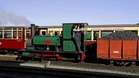 Ffestiniog-Railway---engineer-shunts-LILLA-narrow-gauge-steam-engine-backwards-with-truckloads-of-coal,-Porthmadog-Harbour-Railway-Station,-Snowdonia,-Wales---man-in-cap,-SLOMO-60fps