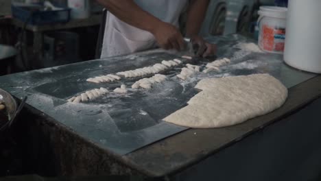 Street-food-merchant-cutting-dough-to-make-deep-fried-dough-sticks,-street-food-in-Thailand