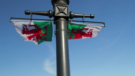 Bandera-De-Gales---Baner-Cymru---Dos-Banderas-Galesas-Ondean-En-La-Brisa-Con-Un-Cielo-Azul-Profundo-Detrás,-Slomo-60fps
